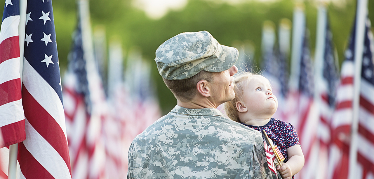 Military man holding his daughter and looking at the American flags all around them