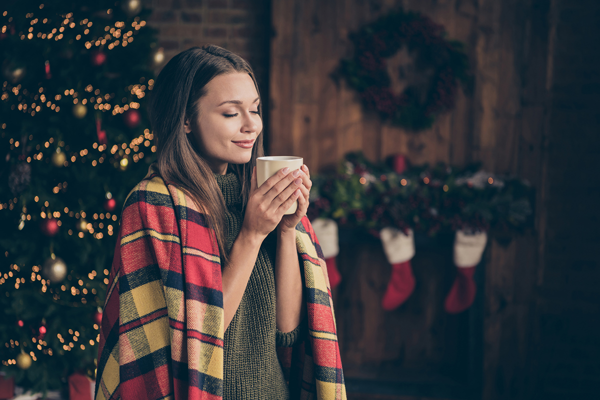 Profile side photo of dreamy positive woman covered checkered blanket feel pleasure on christmas time vacation hold mug smell hot beverage in house with x-mas ornament wreath red socks indoors - All is calm, all is bright: Managing your Mental Health at Christmastime